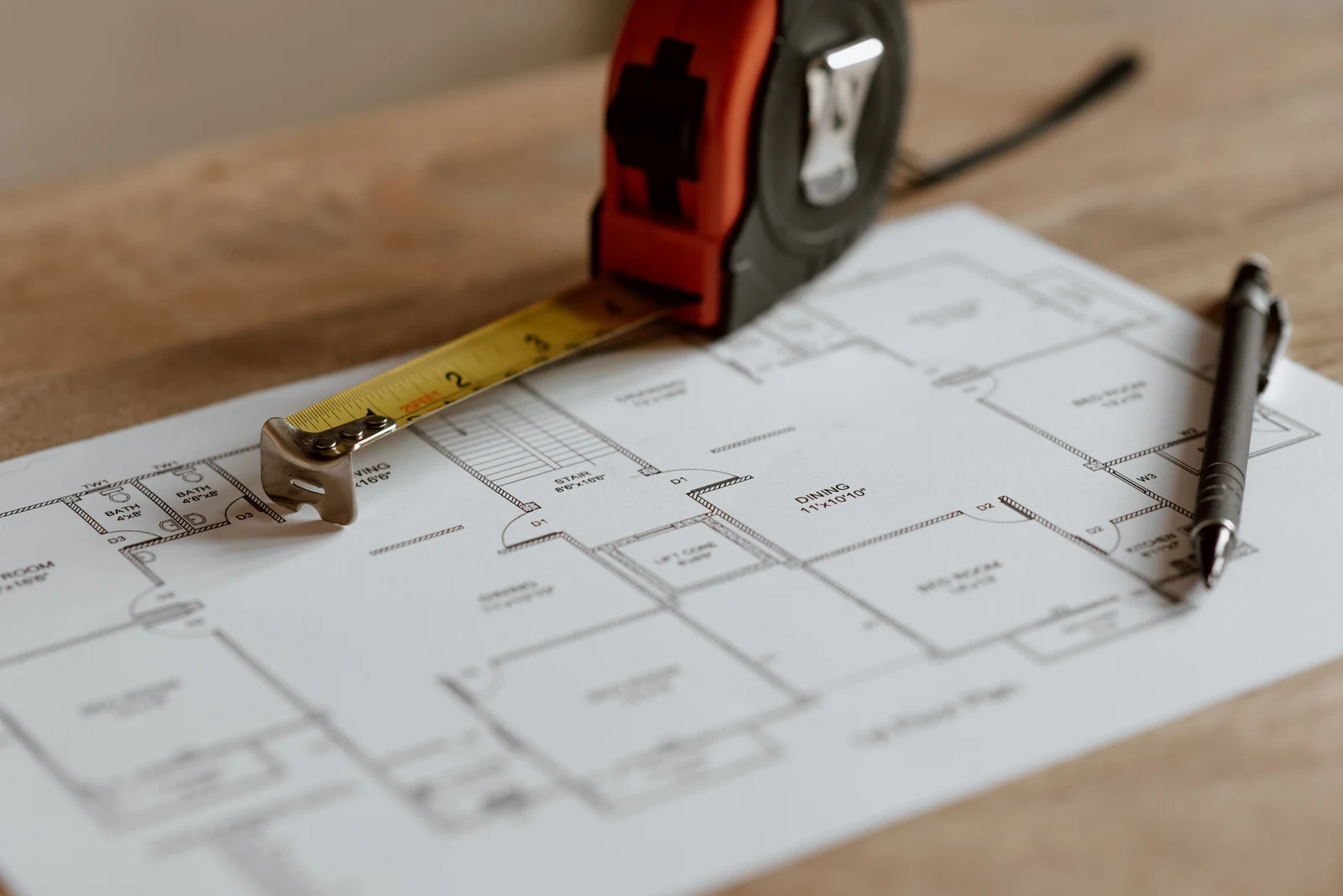A tape measure and pen laid across an architectural floor plan